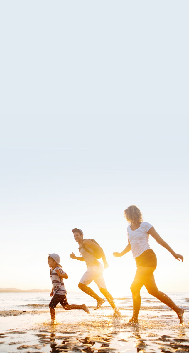 A man, woman, and child running on a beach with the sunsetting in the background.